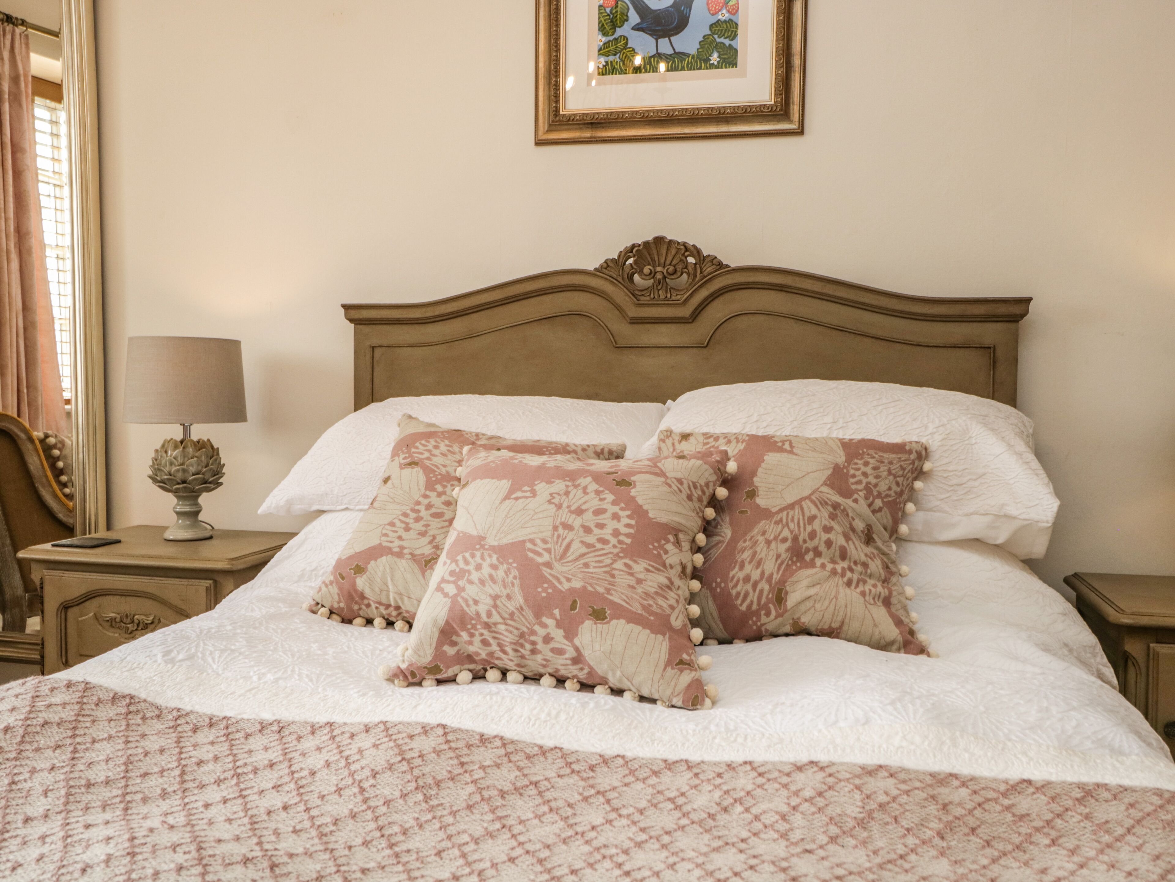 A neatly made bed with floral patterned pillows and a white comforter, a bedside lamp, and a framed picture on the wall.