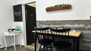 Een kamer met een houten tafel en twee zwarte stoelen, een witte tafel met een klein voorwerp erop, en een bord met een welkomstboodschap aan de muur.
