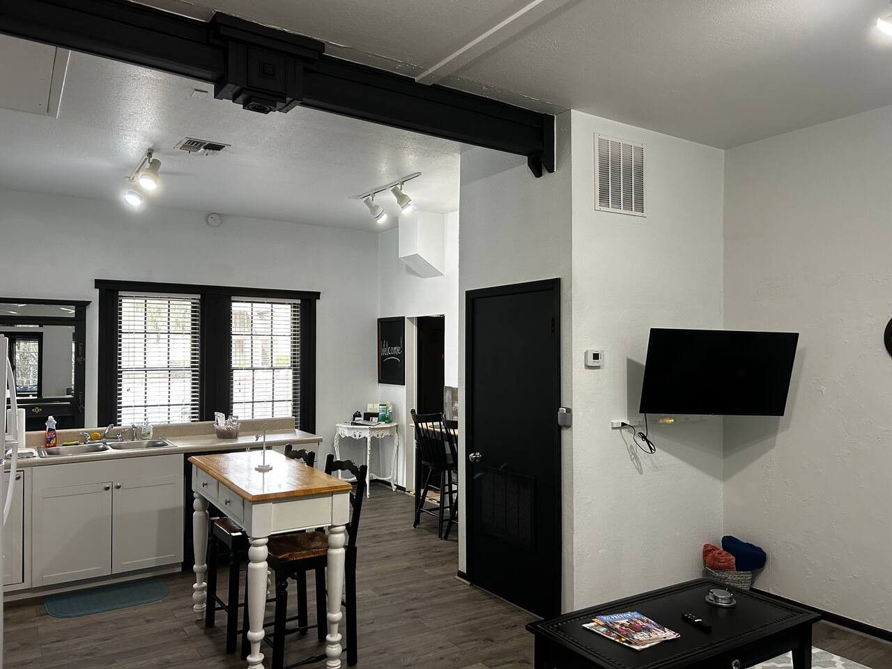 Cozinha compacta com área de refeições, TV fixada na parede e porta que dá para outro quarto.