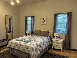 Un dormitorio con una cama, dos mesitas de noche, un espejo y un ventanal con cortinas.