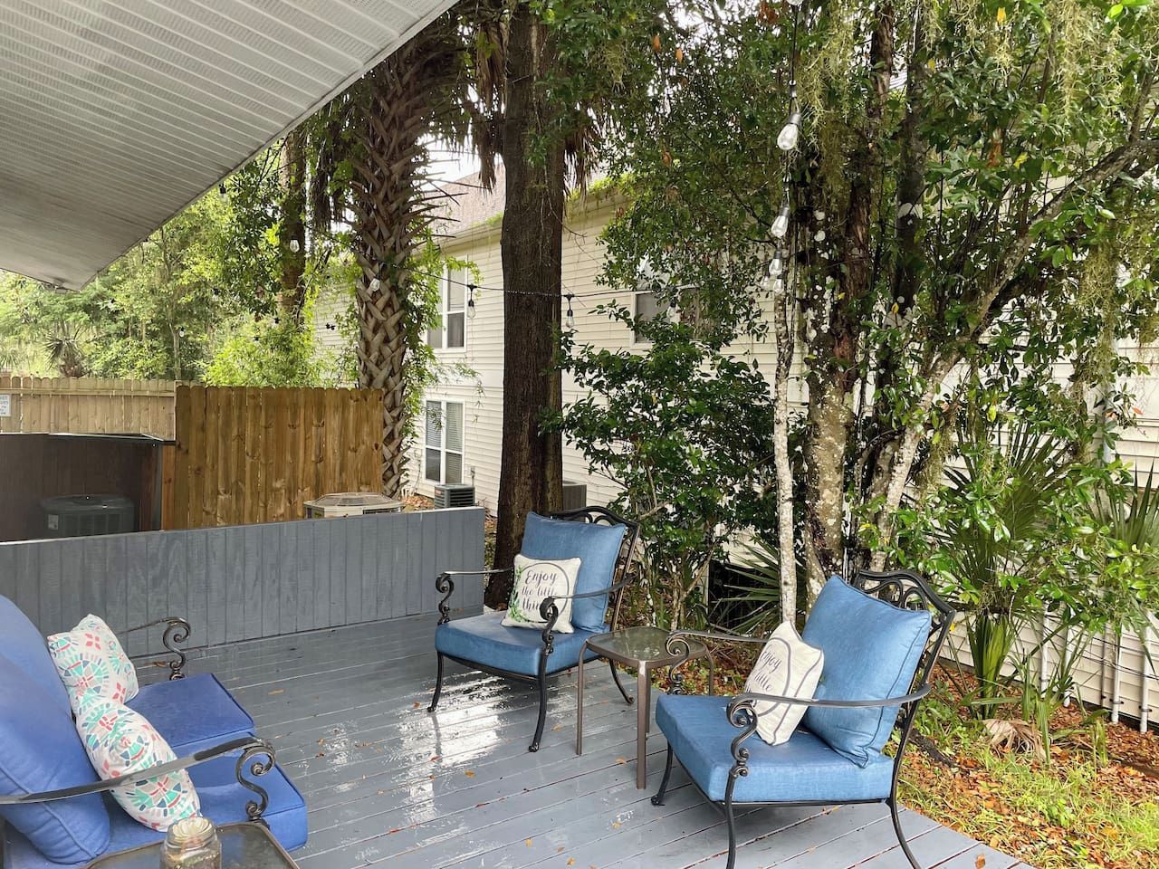 An outdoor patio with blue chairs and a table, surrounded by trees and a wooden fence.