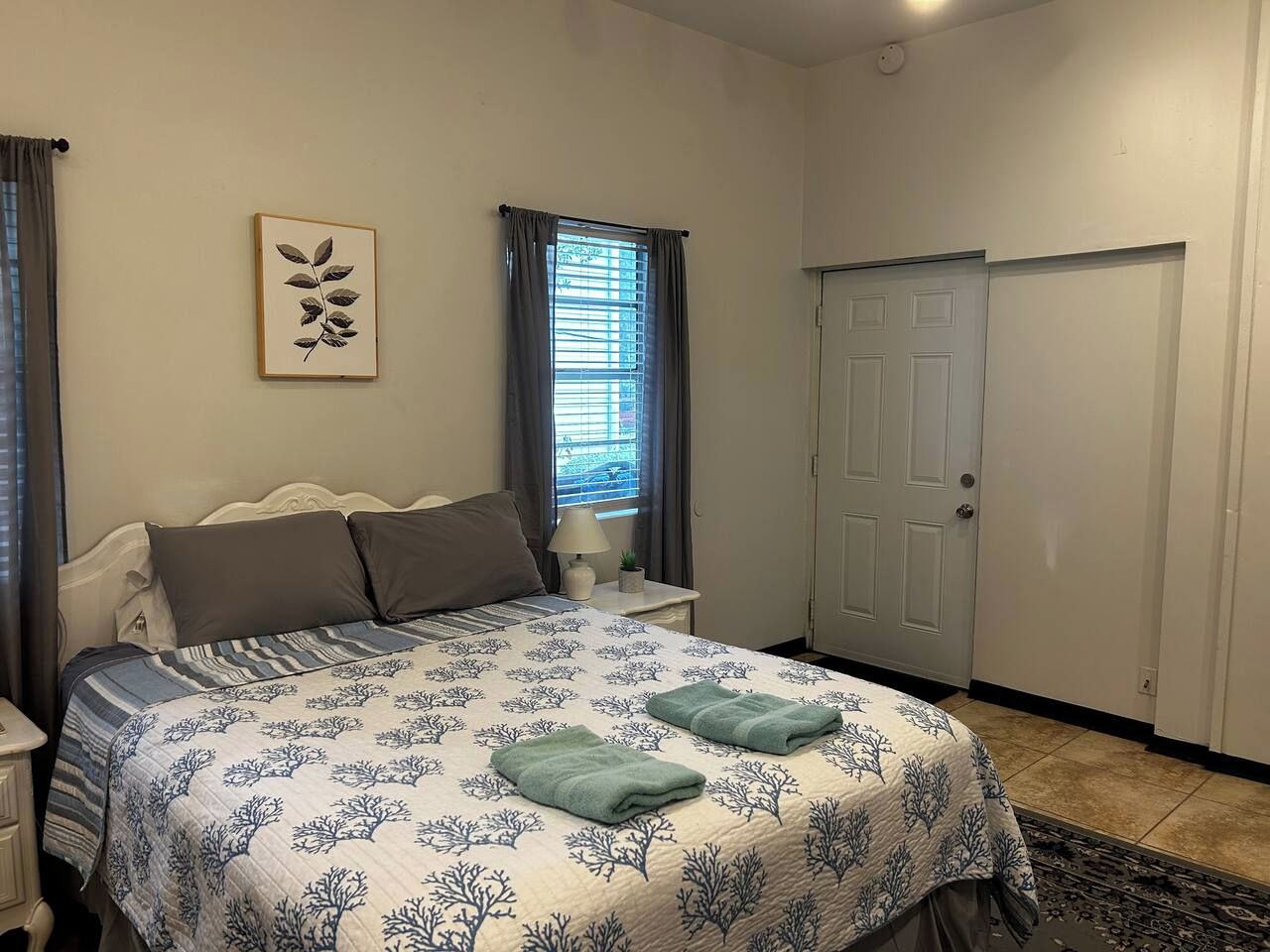 A bedroom with a bed, curtains, a door, and a wall-mounted picture.