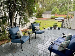 A wooden deck with outdoor furniture, including chairs and a sofa, surrounded by greenery and a white fence. - Kemp House Magnolia Suite | Historic Charm Downtown Ocala (Ocala)