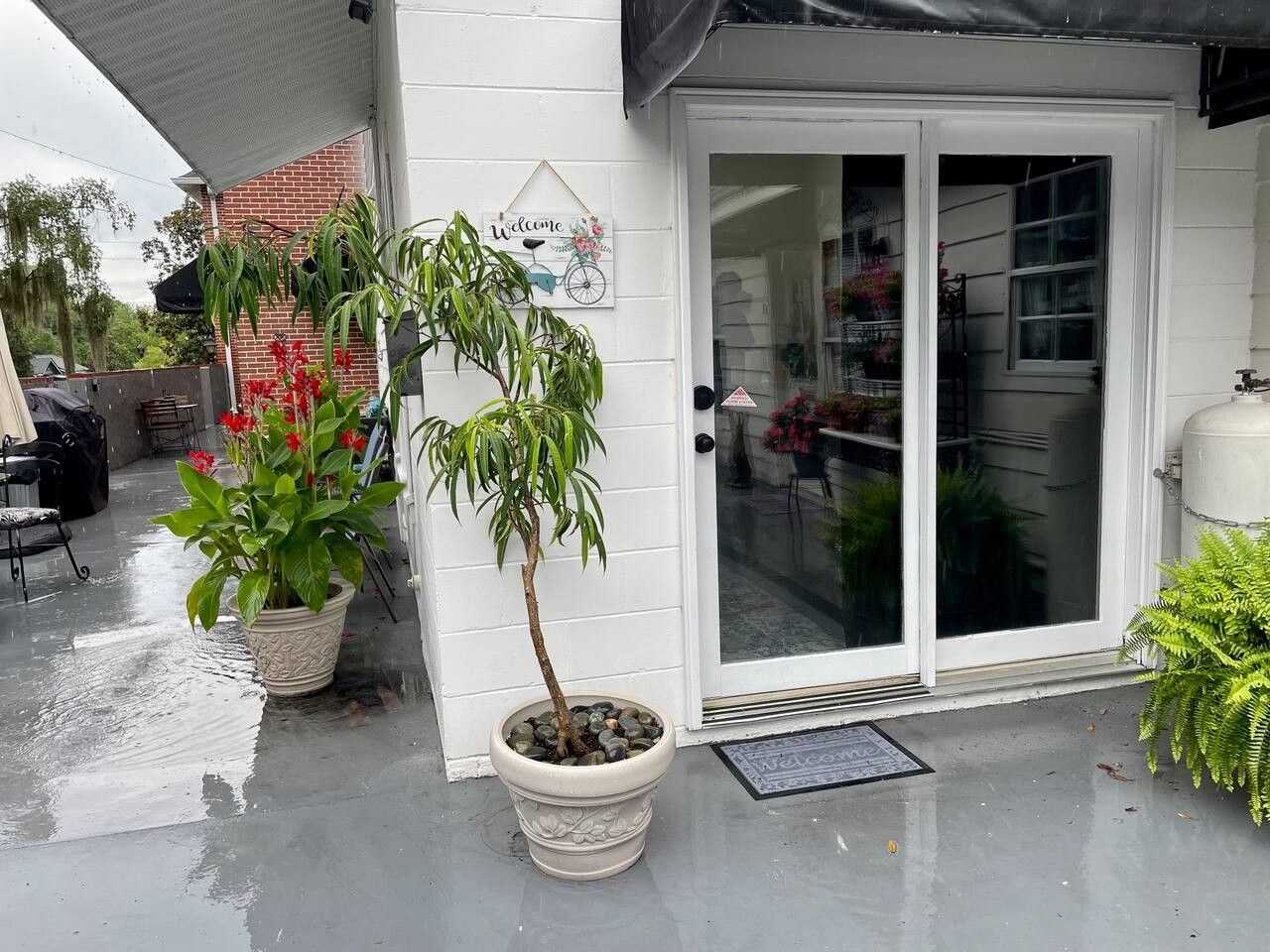 A white building with a glass door entrance, potted plants, and a welcome sign.