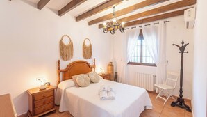 A bedroom with a wooden bed, bedside tables, a chandelier, a radiator, and a window with curtains.