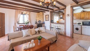 A cozy living room with a sofa, dining table, and chairs, a kitchen with a brick wall, and a laundry area.