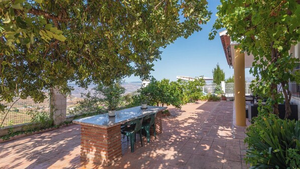 An outdoor patio with a brick barbecue area, potted plants, and a view of the cityscape.