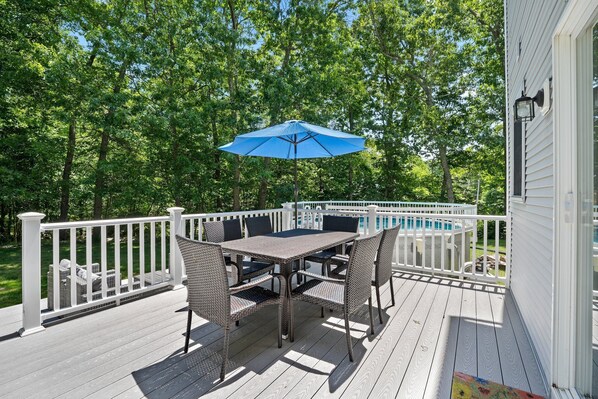 A deck with a table and chairs, a blue umbrella, and a pool in the background.