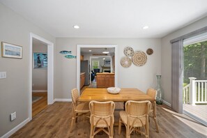 A dining area with a wooden table and wicker chairs, a kitchen in the background, and decorative wall art.
