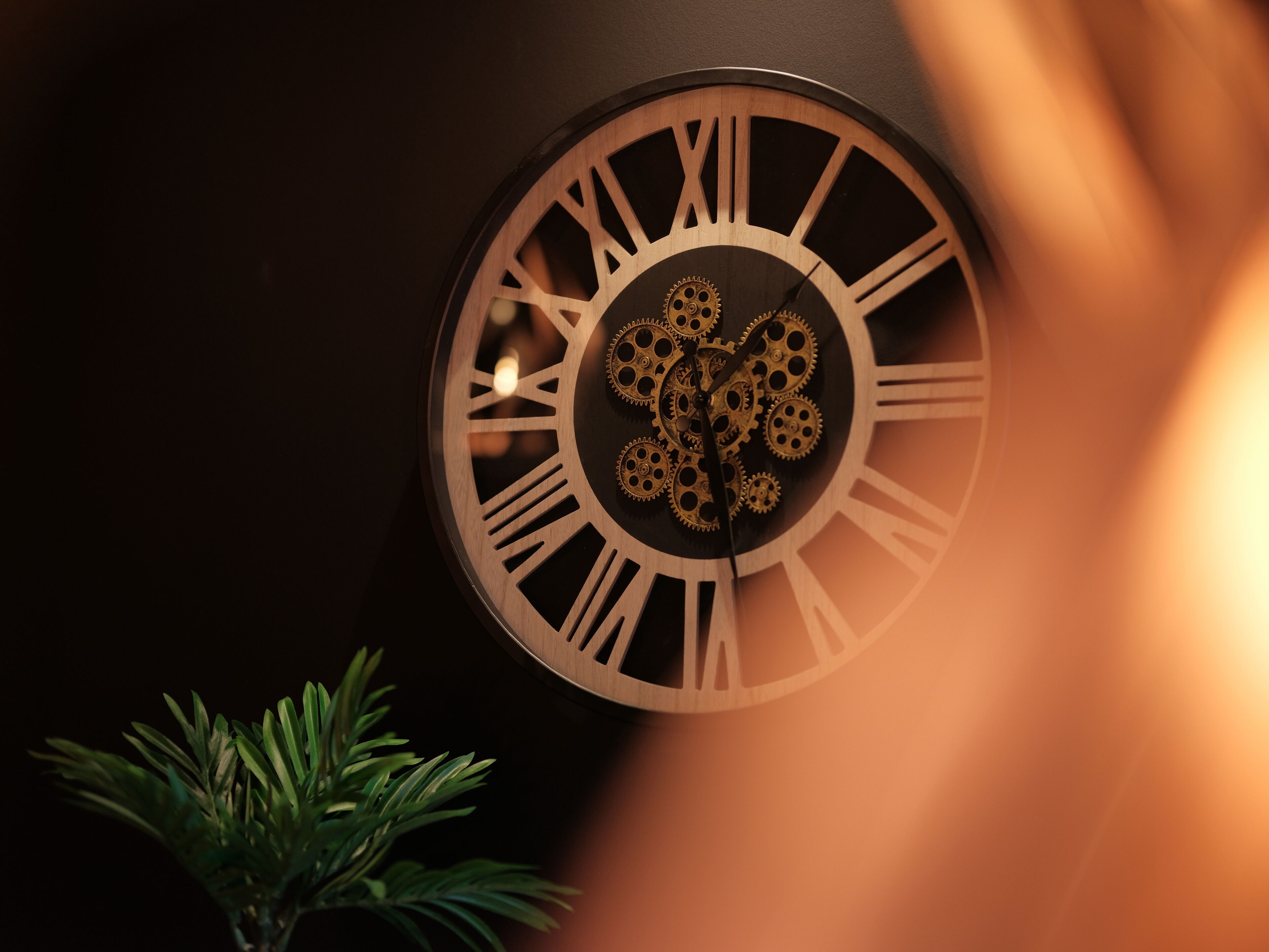 A wall clock with Roman numerals and gears, mounted on a dark wall.