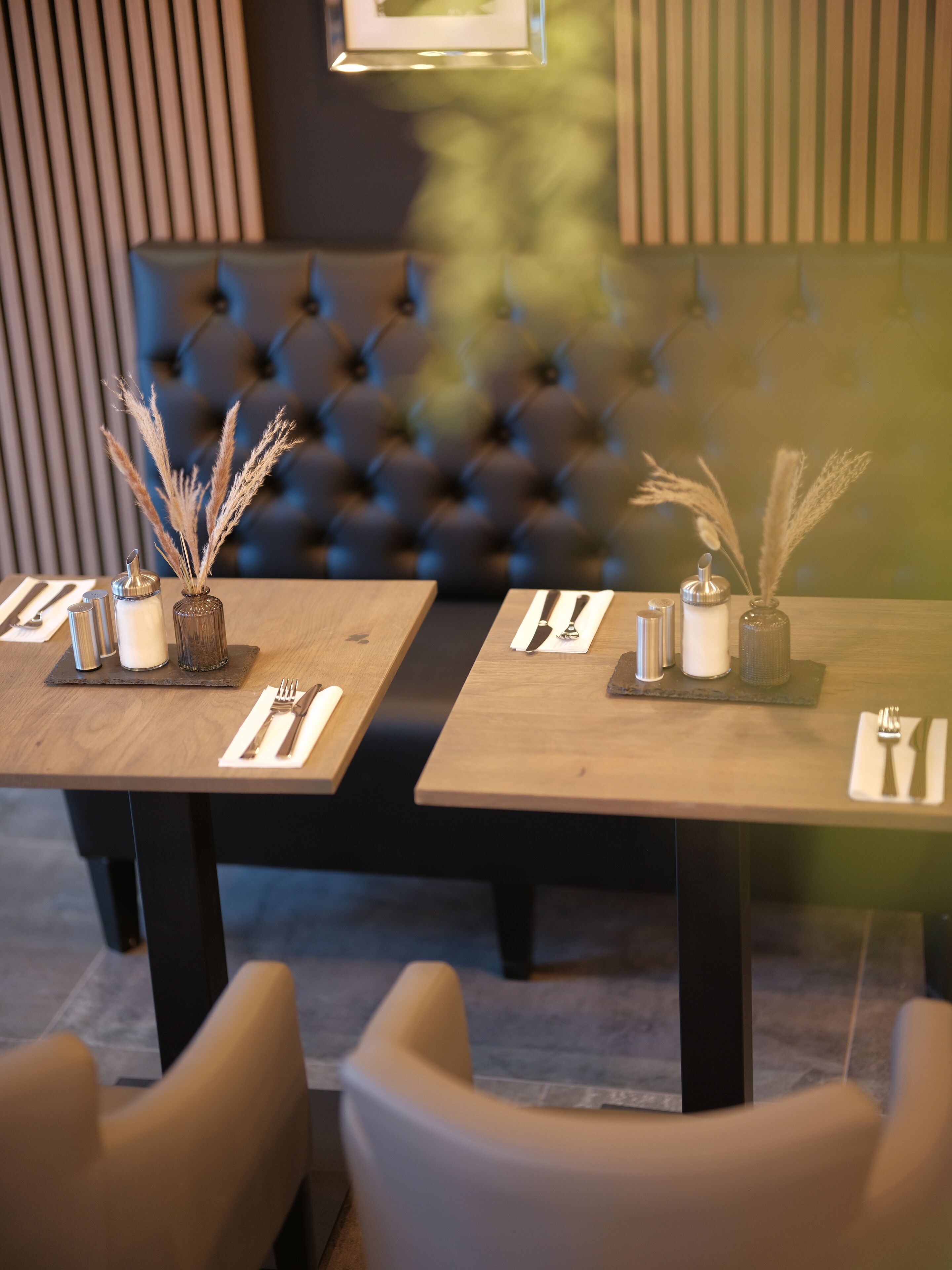 Una sala da pranzo con due tavoli, ognuno apparecchiato con posate, tovaglioli e vasi decorativi.