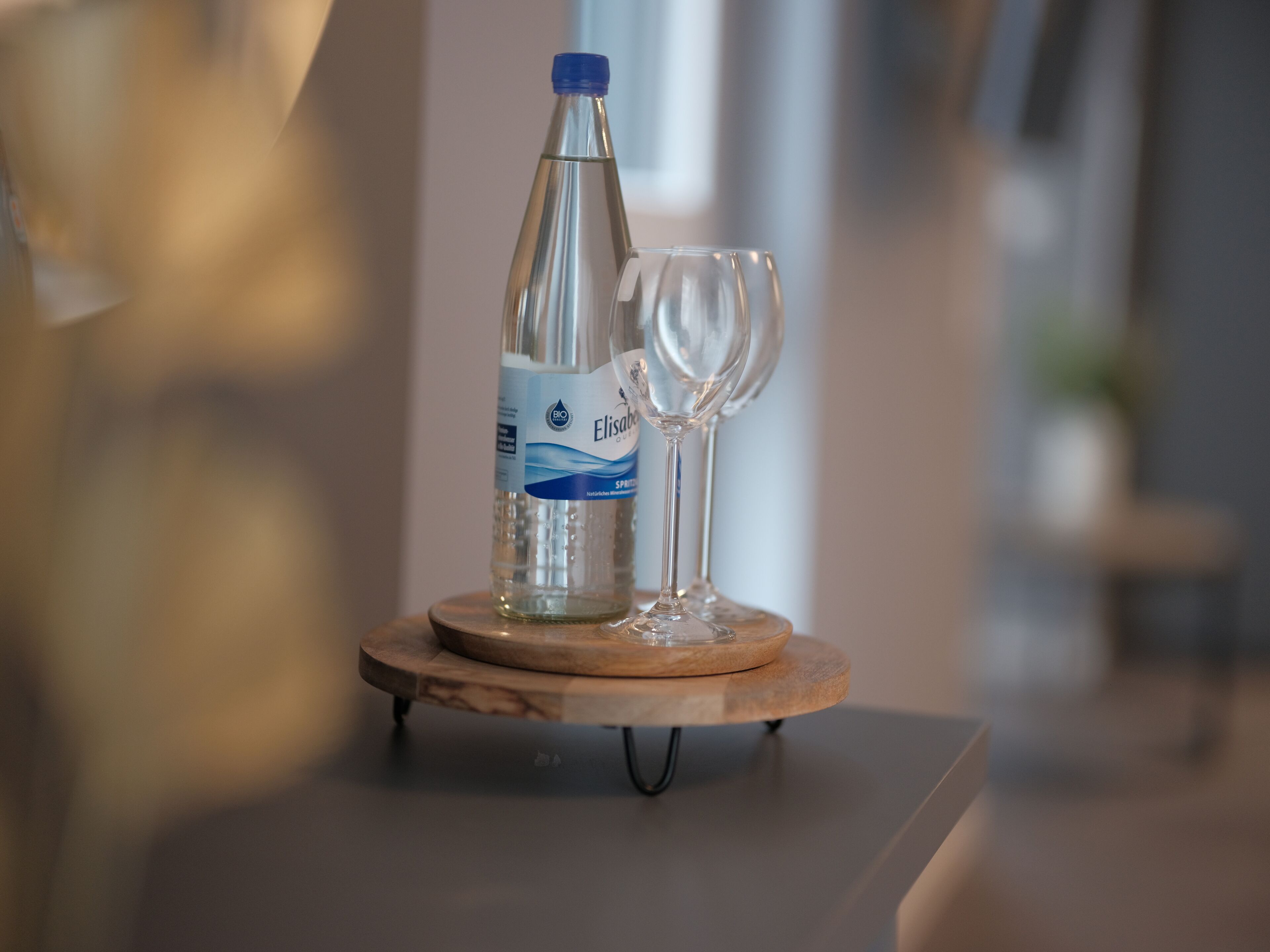 Een fles Elisabé water en een wijnglas op een houten onderzetter.