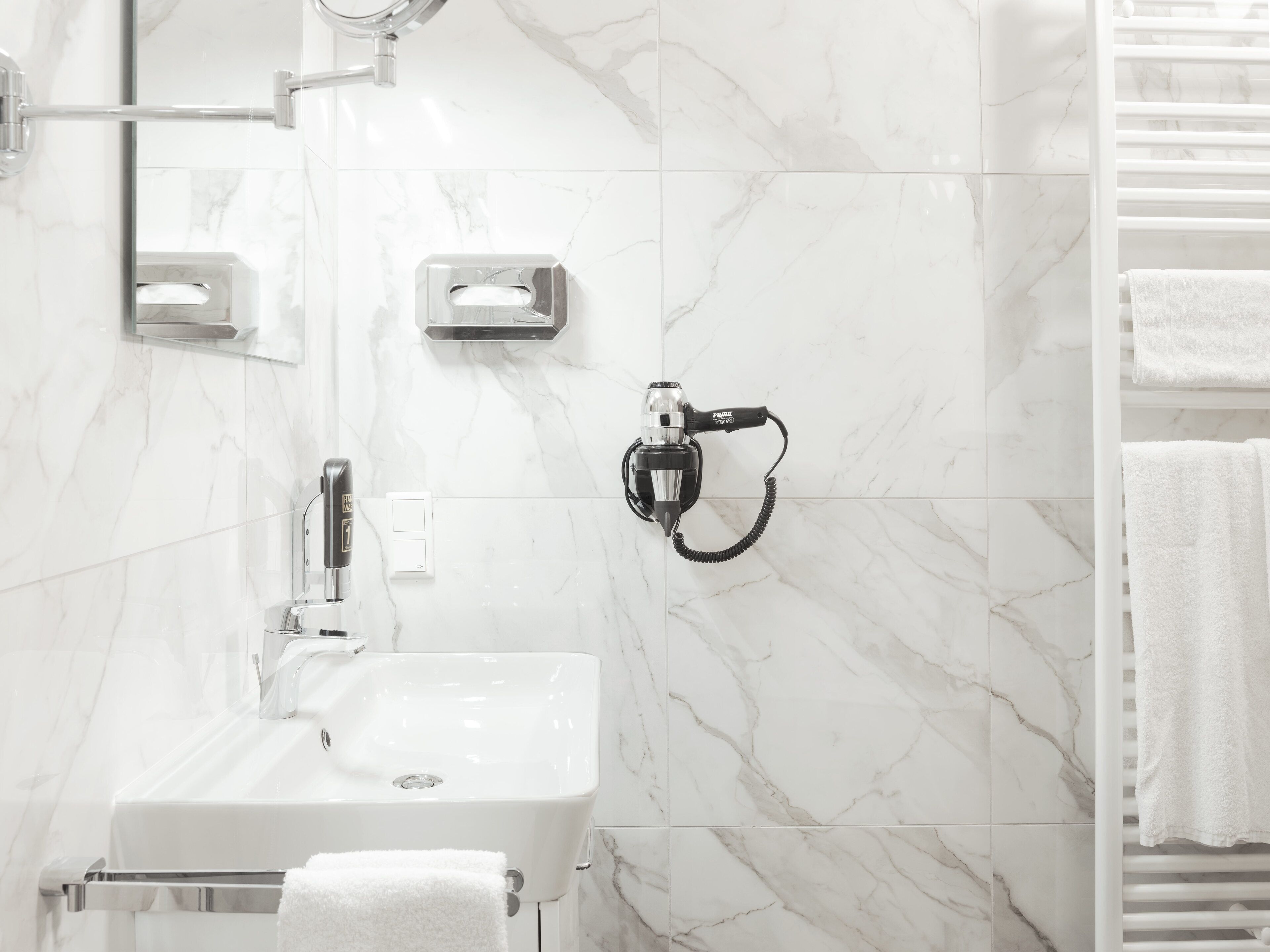 A bathroom with a white sink, a handheld showerhead, and a towel rack.