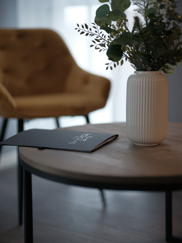 Una habitación moderna con una mesa redonda de madera, una planta en maceta y una carpeta negra.