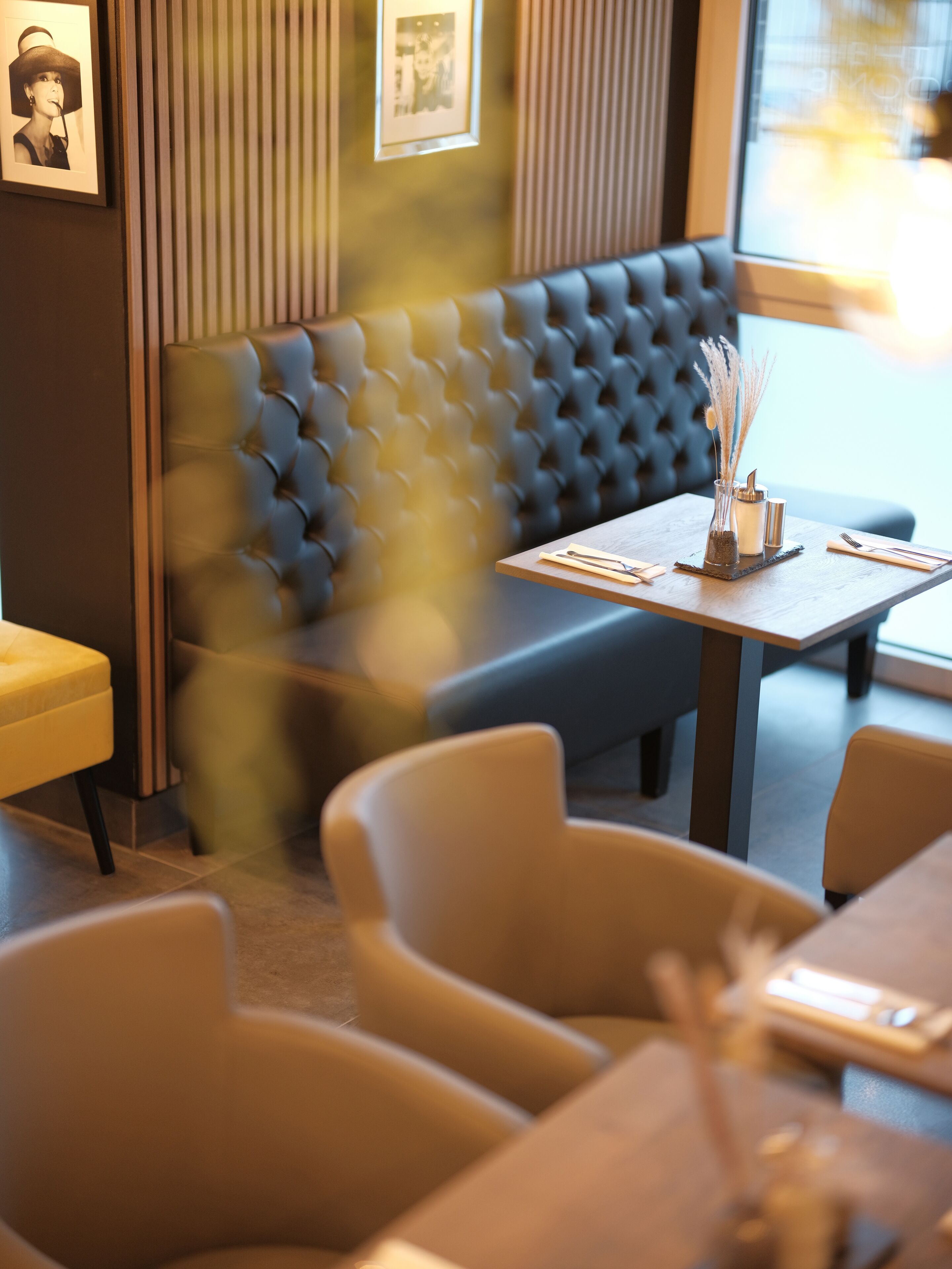 Een restaurantinterieur met een blauwe, gestofte zithoek, houten tafels en stoelen.