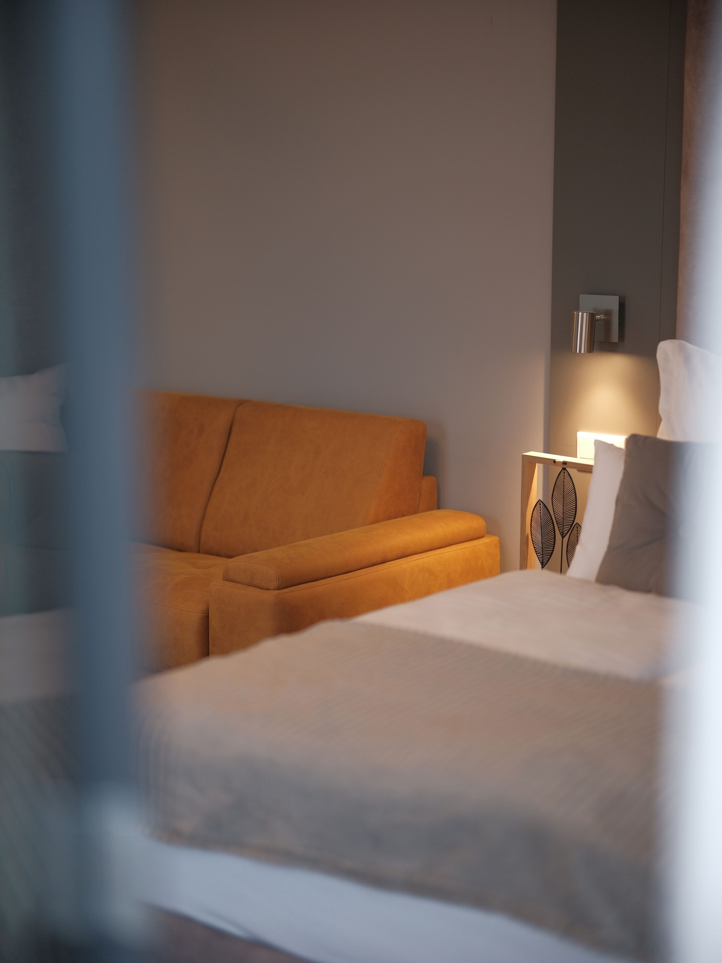 A modern hotel room with a large bed, an orange sofa, and a bedside table with a lamp.