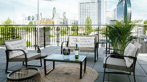 A balcony with wicker furniture, a glass table, and a large umbrella. - THE ROOMS - Hotel & House (Frankfurt)
