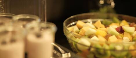 A bowl of fruit salad with a variety of fruits and a glass of a creamy beverage.