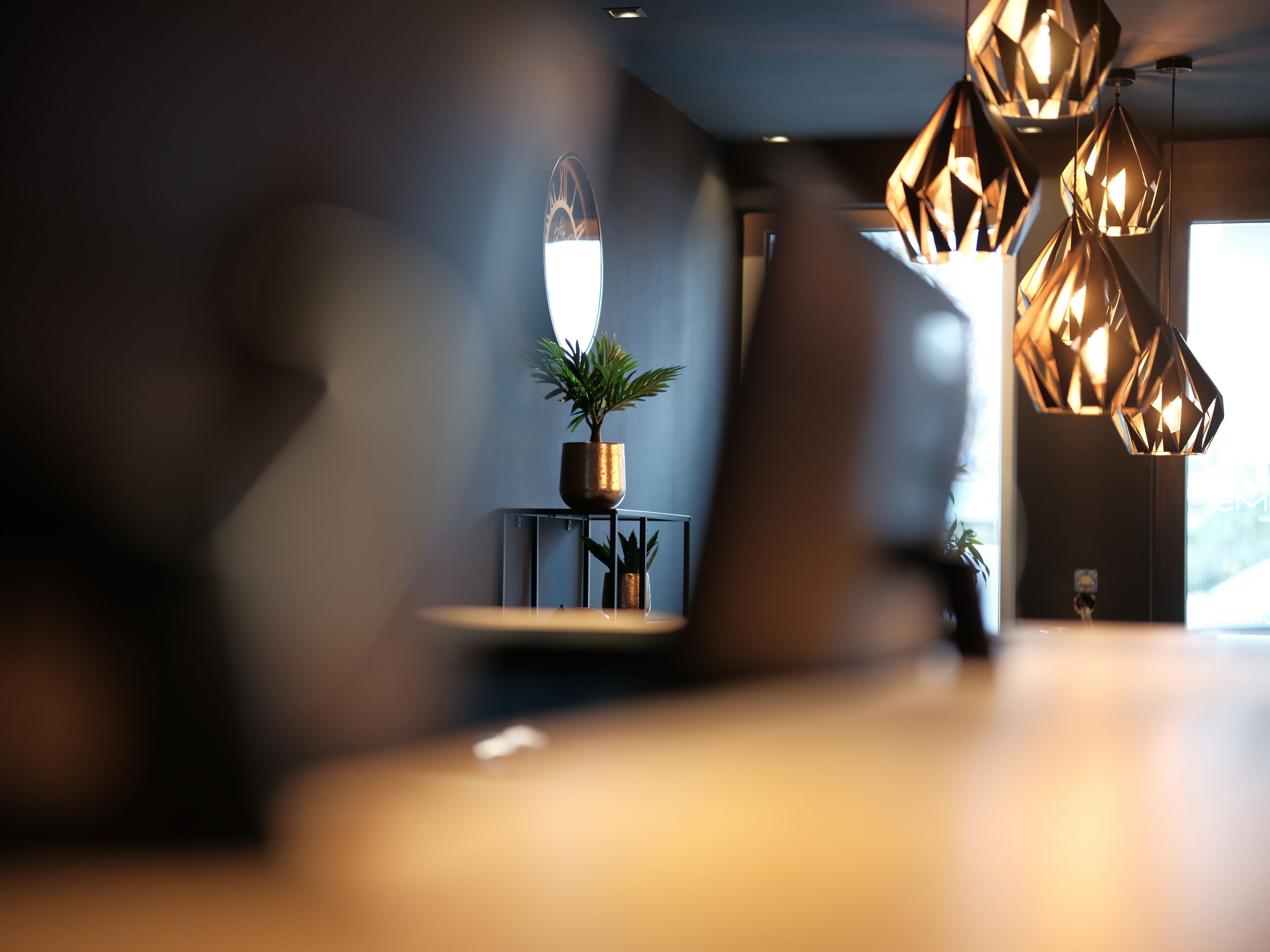 A modern interior with geometric pendant lights, a potted plant on a small table, and a reflective surface.