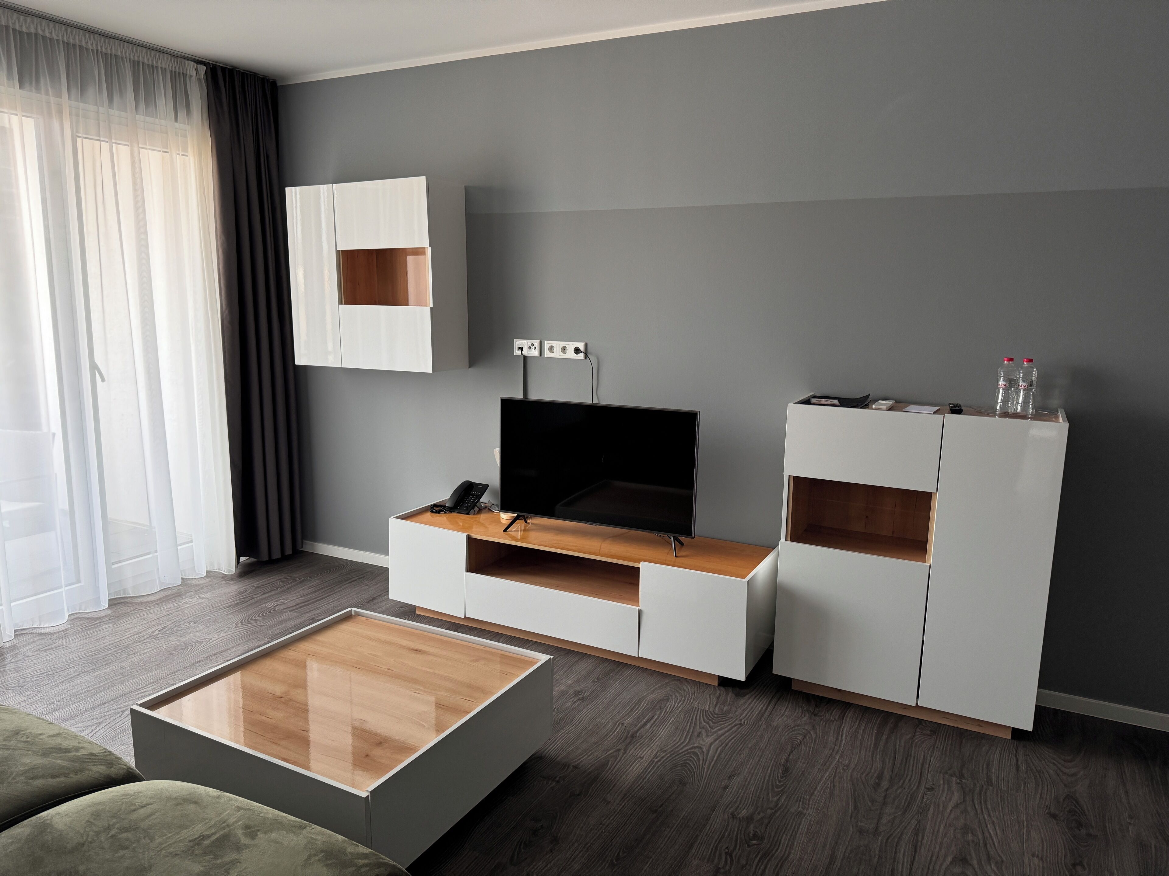 Una sala de estar moderna con un televisor de pantalla plana, una mesa de centro de madera y unidades de almacenamiento empotradas frente a una pared gris.