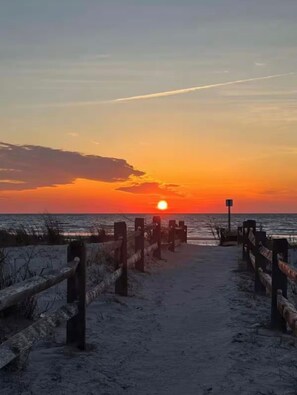 A beach path with wooden railings leading to the ocean at sunset.