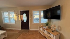 Una sala de estar con un televisor montado en la pared, un mueble bajo de madera y una puerta con un panel de vidrio decorativo.