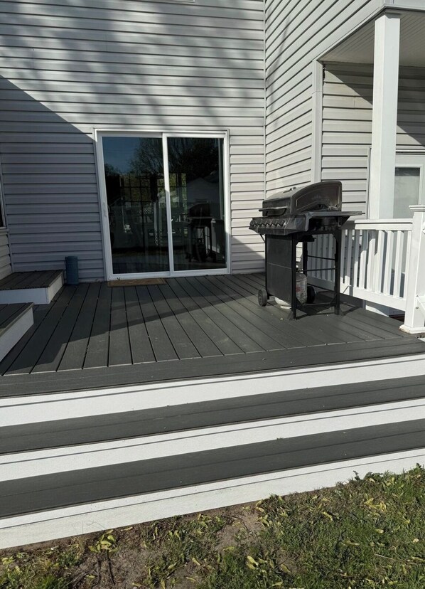A deck with a grill and a sliding glass door leading to a covered patio area.