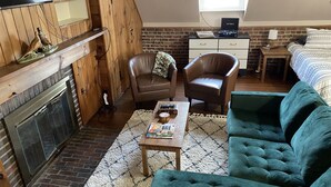 Um quarto acolhedor no estilo loft, com lareira, um sofá verde, uma poltrona de couro e uma pequena mesa de madeira.