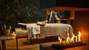 Um espaço de spa com parede de pedra, mesa de massagem, massagista, velas e lareira.