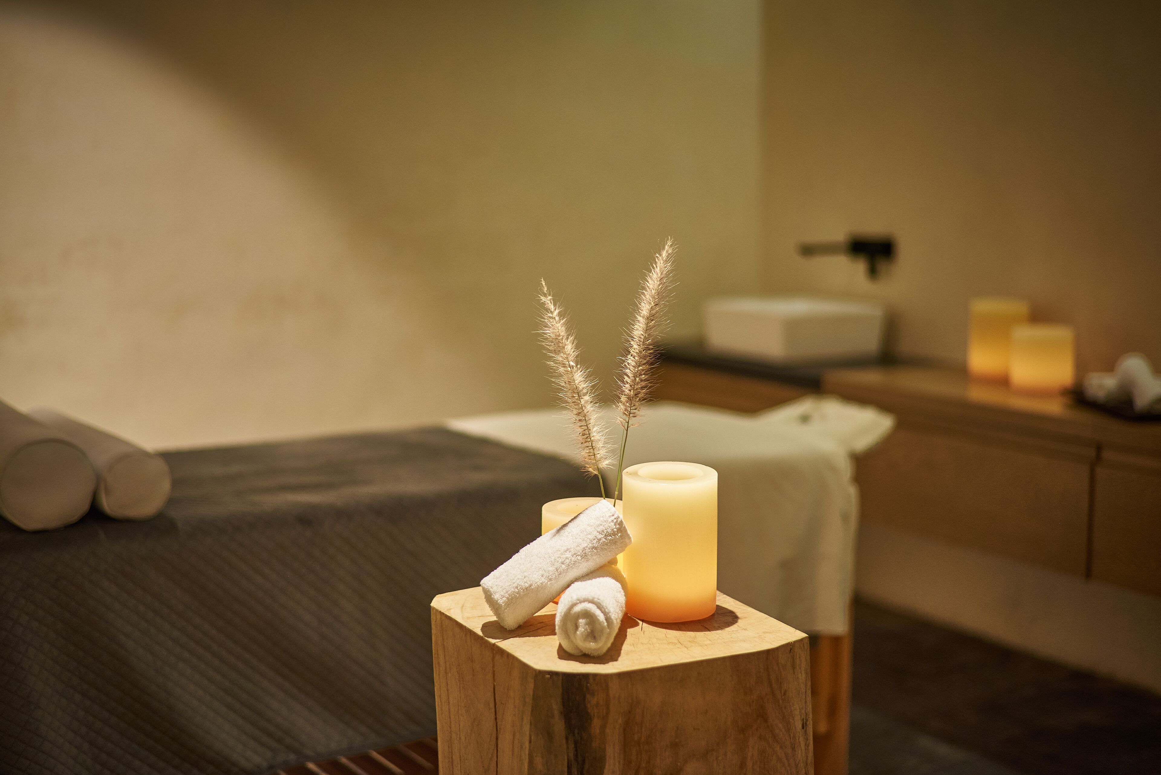 A wooden stool with a candle, rolled towels, and decorative grasses in a spa setting.