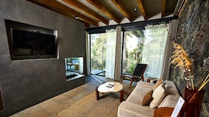 Uma sala de estar moderna com uma televisão grande, um sofá, uma mesa de centro e vista para o exterior.