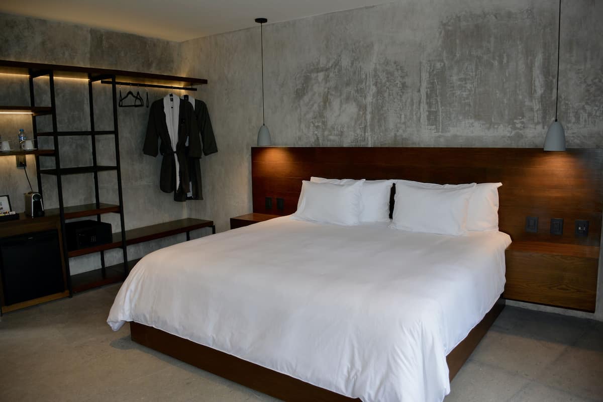 Ein modernes Hotelzimmer mit einem großen Bett, einem Holz-Kopfteil und einem eingebauten Kleiderschrank mit Kleidung.