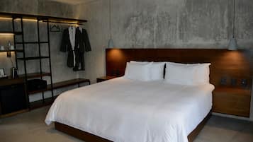 Una habitación de hotel moderna con una cama grande, cabecero de madera y un armario empotrado con ropa colgada.