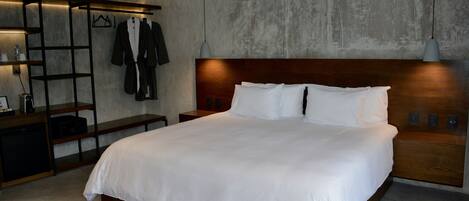 Una habitación de hotel moderna con una cama grande, cabecero de madera y un armario empotrado con ropa colgada.