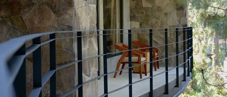 A balcony with a stone wall, a metal railing, and a wooden table and chairs.