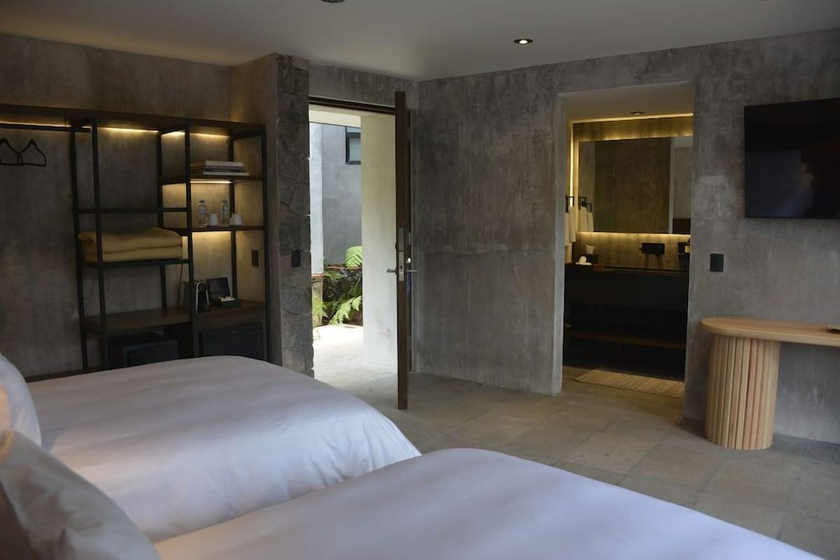A modern hotel room with a large bed, a built-in wardrobe, a bathroom with a mirror, and a TV mounted on the wall.