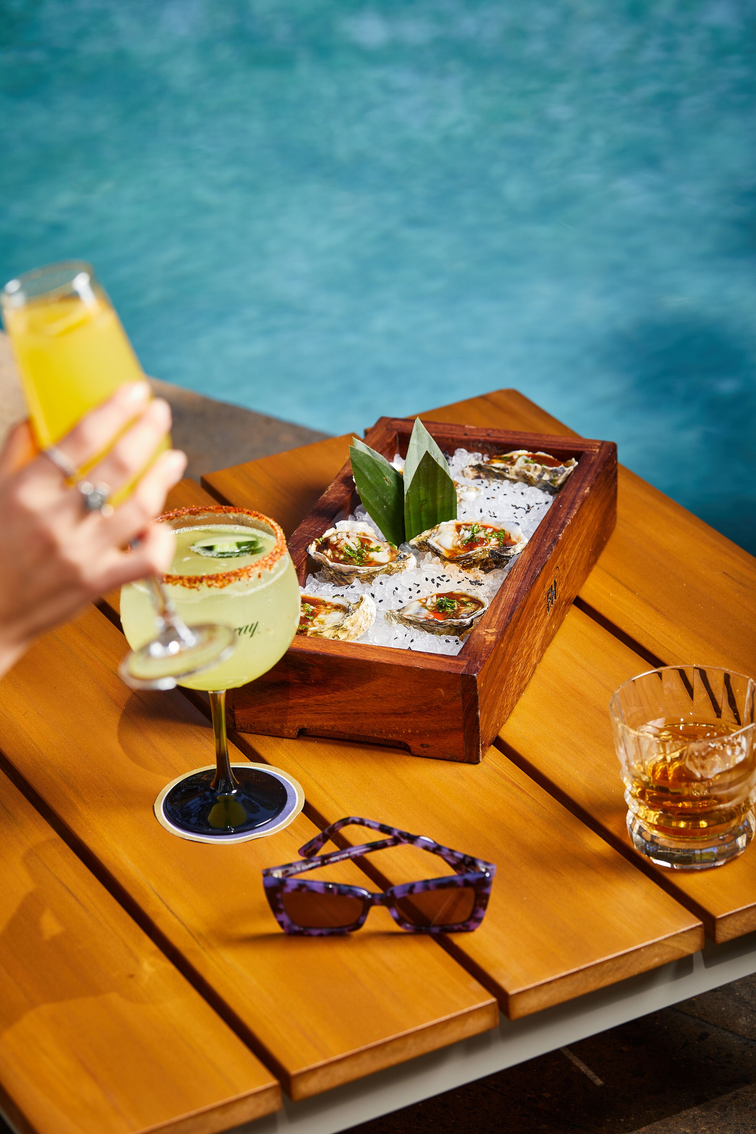 Ett träbord med ett fat ostron, en cocktail och ett glas whisky.