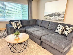 A modern living room with a grey sectional sofa, two patterned throw pillows, a small wooden coffee table, and a framed landscape painting on the wall. - Coastal Naples Home Heated Pool Near Beach (Naples)