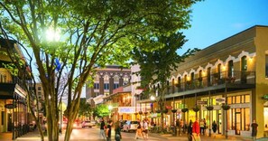 Une rue bordée de boutiques et de restaurants, où l’on croise des piétons et des voitures.