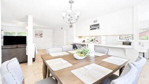 A modern dining area with a wooden table, six chairs, a chandelier, and a welcome sign.