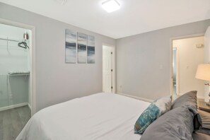 Une chambre à coucher avec un lit, une table de chevet, une lampe et une porte donnant sur une autre pièce.