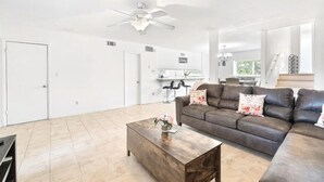A spacious living room with a dark brown leather sofa, a wooden coffee table, and a ceiling fan.