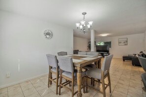 Un coin repas avec une table et des chaises en bois, un lustre, une horloge et un téléviseur en arrière-plan.