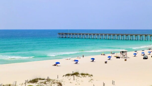 A beach with a pier extending into the ocean, sandy beach, and several umbrellas.
