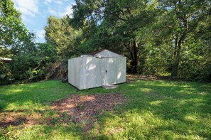 A small, single-story shed in a grassy yard surrounded by trees.