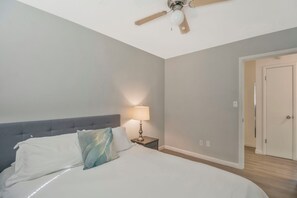 A bedroom with a bed, a nightstand, a lamp, a ceiling fan, and a door.