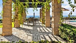 A covered outdoor seating area with stone pillars, a pergola with vines, and a view of the sea. - Exclusive Monarch Beach, Ritz Pointe Condo - 2 Bedroom, 2 Bath [STR23-0012] (Dana Point)