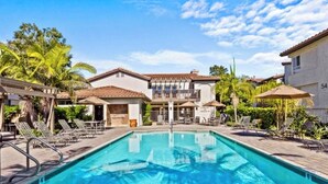 A swimming pool with lounge chairs, a covered seating area, and a building with a balcony. - Exclusive Monarch Beach, Ritz Pointe Condo - 2 Bedroom, 2 Bath [STR23-0012] (Dana Point)