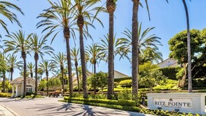A paved pathway lined with palm trees and a sign for Ritz Pointe Communities. - Exclusive Monarch Beach, Ritz Pointe Condo - 2 Bedroom, 2 Bath [STR23-0012] (Dana Point)