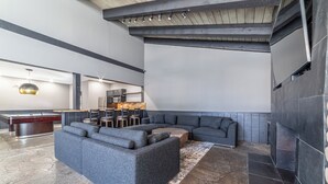 A modern living room with a sectional sofa, a pool table, and a kitchen area in the background.